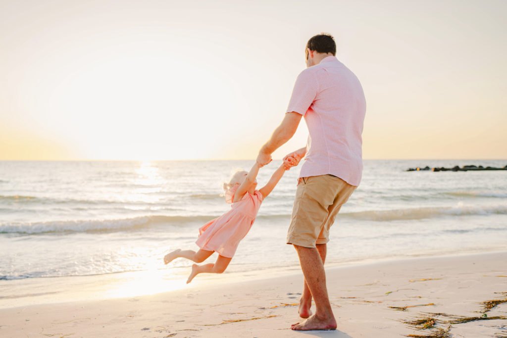florida dad swings child at honeymoon island state park at sunset