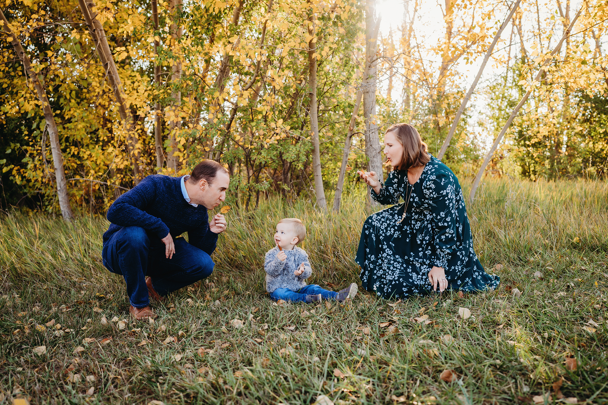 Denver family photographers capture photo of mom and dad blowing kisses at son in front of autumn leaves.