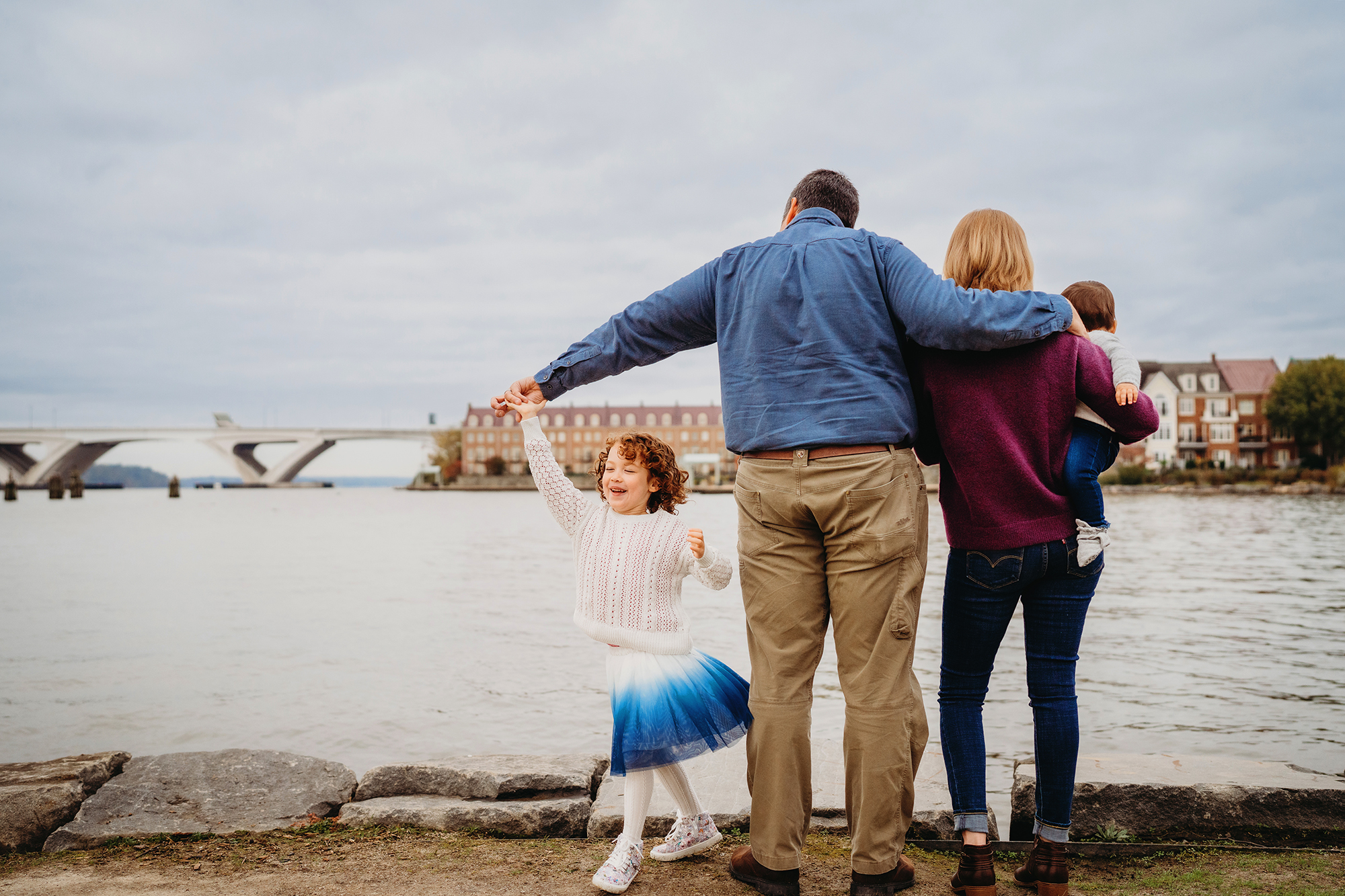 As the family faces the waterfront, a little girl twirls in a blue skirt captured by Denver family photographers