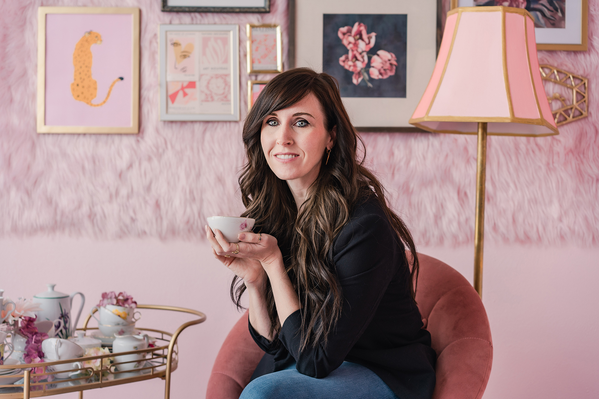 brunette woman sits on pink chair holding teacup in room decorated in pink