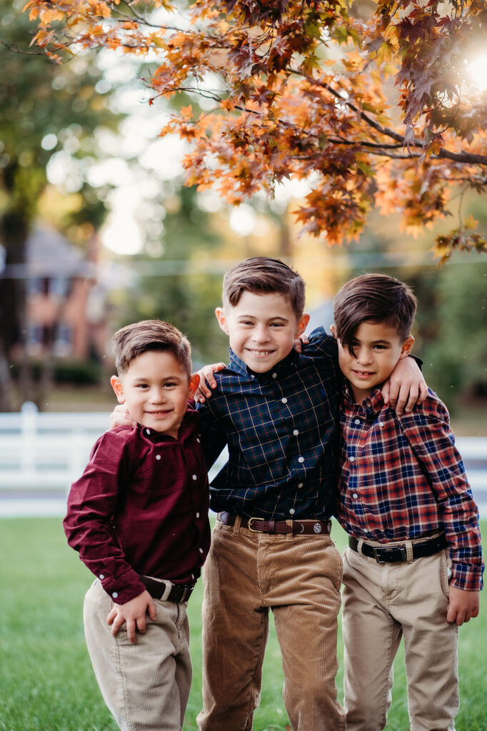 Three young boys put their arms around each others shoulders under glittery fall leaves in a photo by Denver family photographers