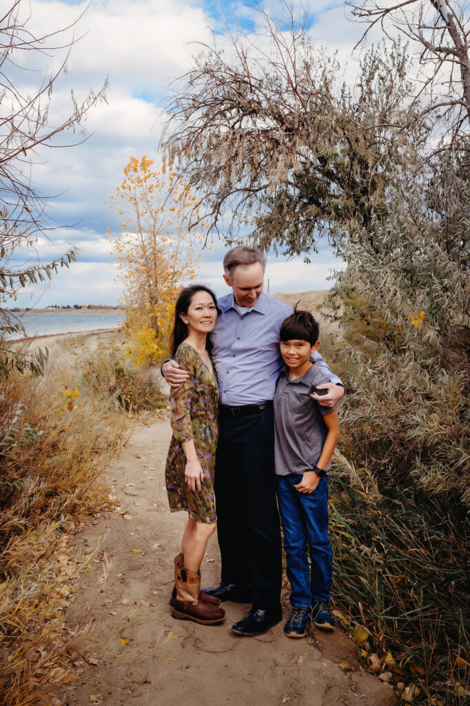 Denver family photographers photograph a family of three standing together on a beach path surrounded by brush