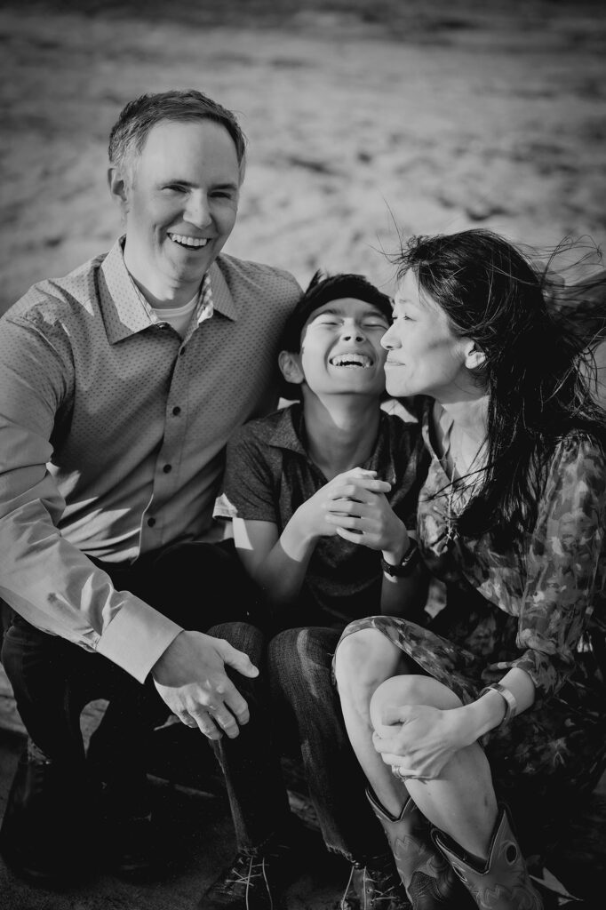 Denver family photographers take a black and white portrait of a family of three laughing on a beach