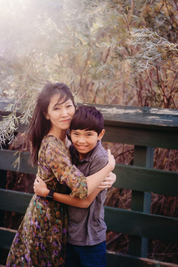 A mother and son smile together as they hug on a bridge in a photo by Denver family photographers