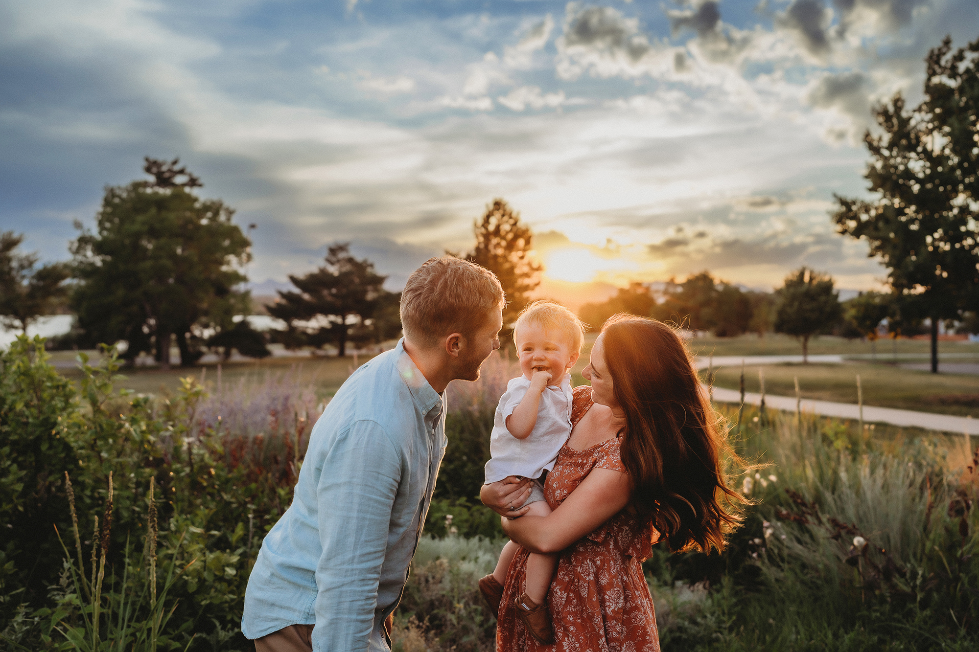 denver family photographers captures young family together in a field cuddling each other as the sunsets in the distance for their denver family photos