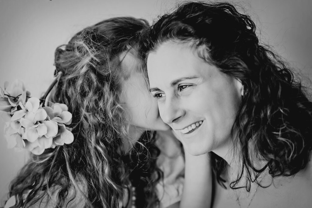 mothers day photos with daughter whispering in her moms ear as the mom smiles and laughs captured by denver family photographer