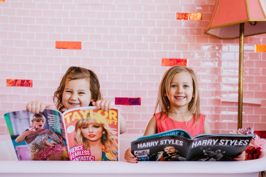 Denver family Photographers captures mothers day mini sessions with two daughter sitting a tub while wearing hot pink matching dresses while holding up pop magazines