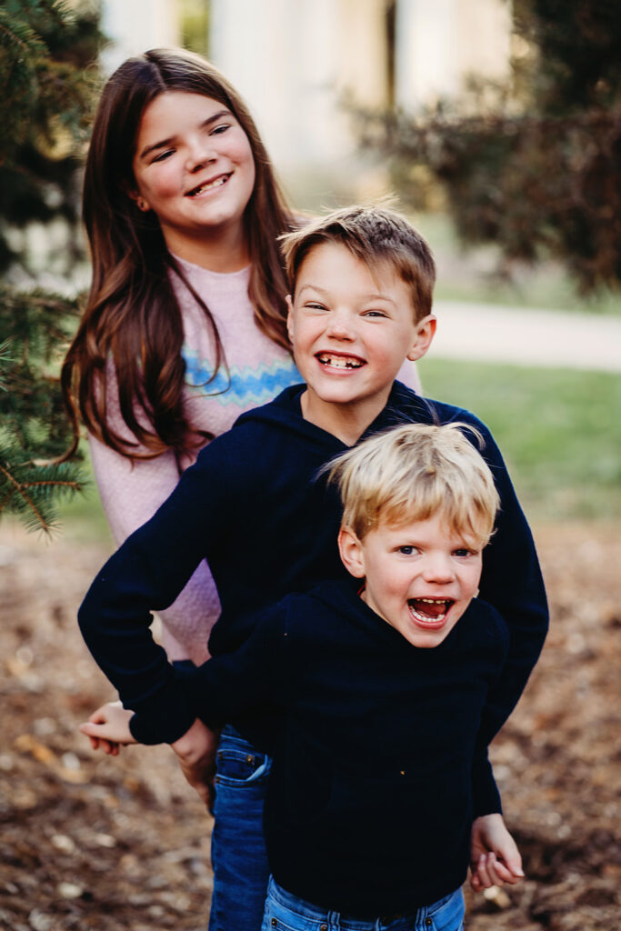 denver family photographers captures siblings pictures with the tallest standing in the back and shorter children standing in front as they all laugh and smile for their outdoor family photos