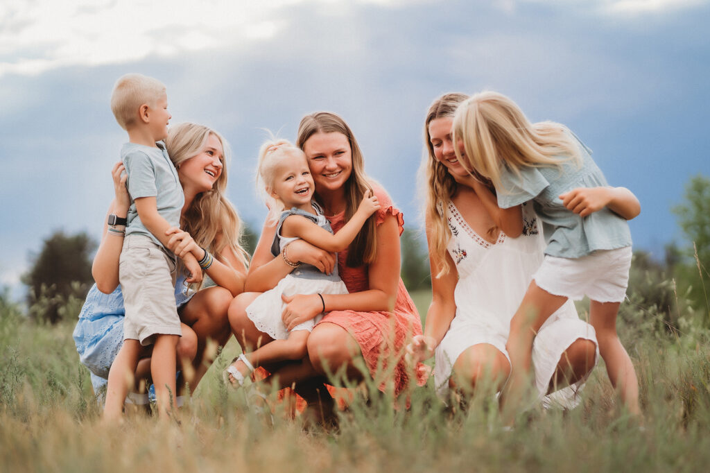 outdoor family pictures with siblings sitting together in a field and hugging one another captured by denver family photographers