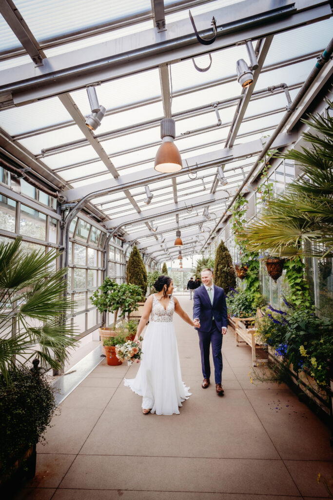 Denver Botanical Gardens wedding venue with bride and groom holding hands and walking through a greenhouse together as the bride looks back over her shoulder to the groom captured by colorado elopement photographer