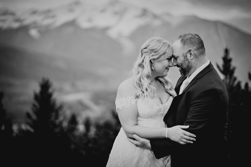 Colorado elopement photographer captures black and white image of bride and groom embracing int he mountains while holding each other and resting their foreheads together