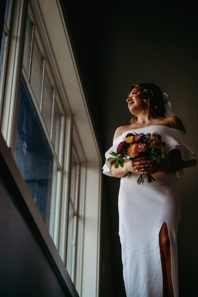 Colorado elopement photographer captures bride holding bouquet looking out window before intimate elopement ceremony