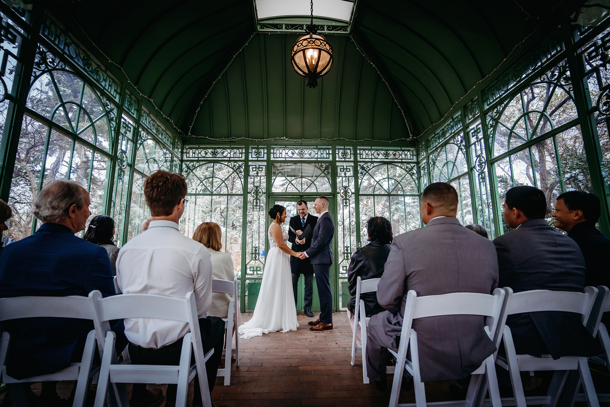 greenhouse wedding ceremony with bride and groom holding hands as their officiant marries them in front of their wedding guests fr a Denver wedding