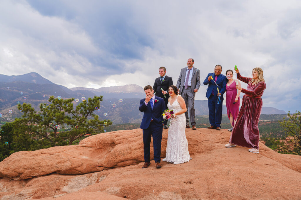 colorado elopement with bride and groom exiting their red rock wedding ceremony as their guests stand behind them and blow bubbles for a bubble exit captured by denver wedding photographer