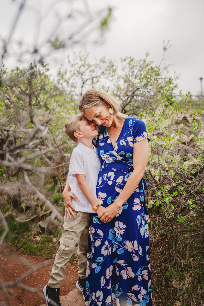 denver family photographers photographer mother in a blue maxi dress holding hands with her young son as he leans up and talks into her ear