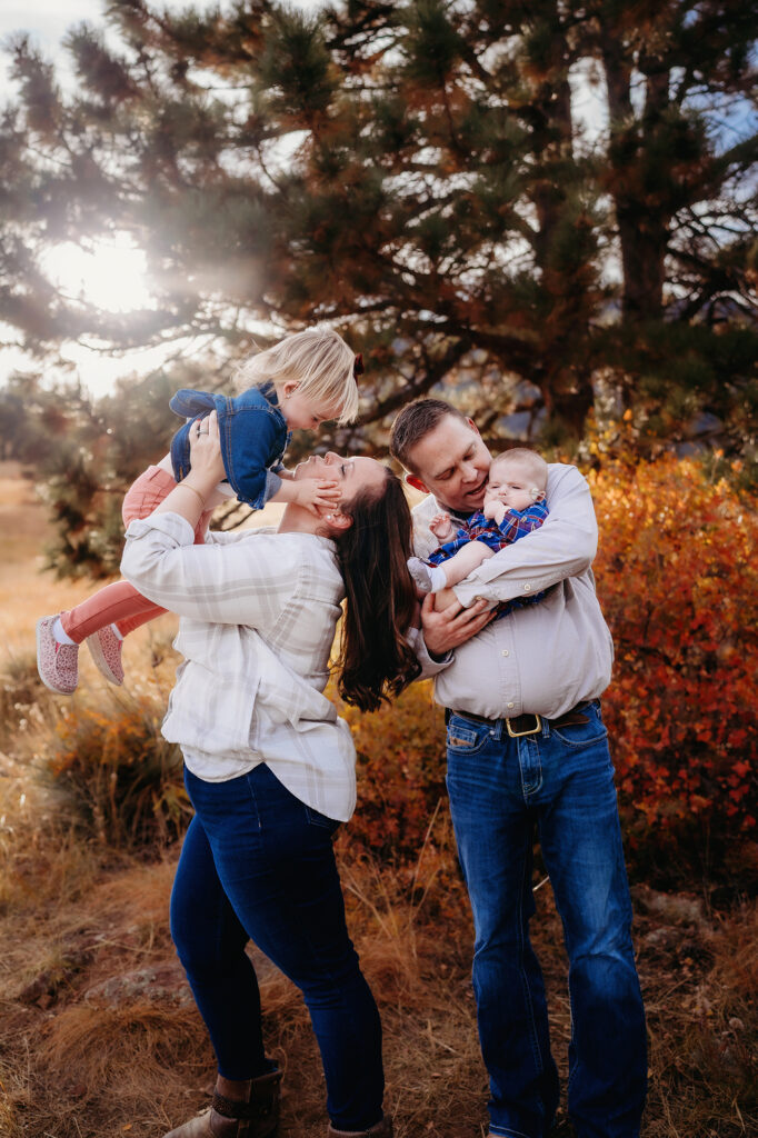 fall family photos with mother tossing little girl in the air and father holding the baby while the sun sets