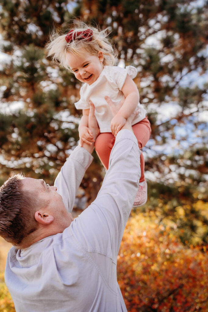 father holding his baby in the air as they play during family photos with denver family photographers