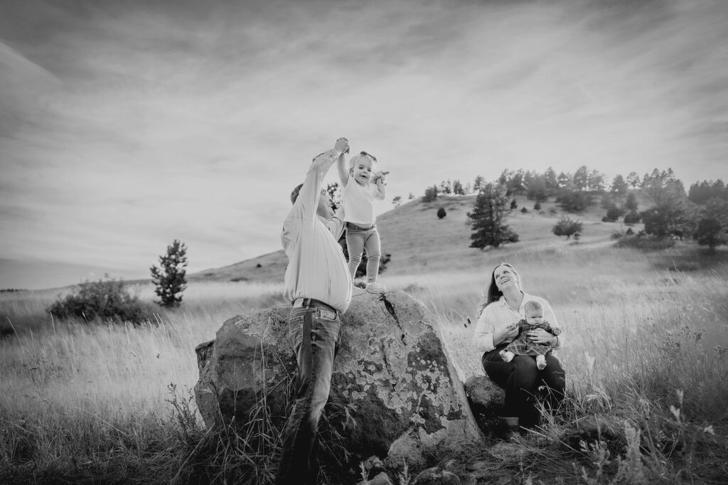 father holding toddler girls hands as she climbs to the top of a bolder during family photos with denver family photogrpahers