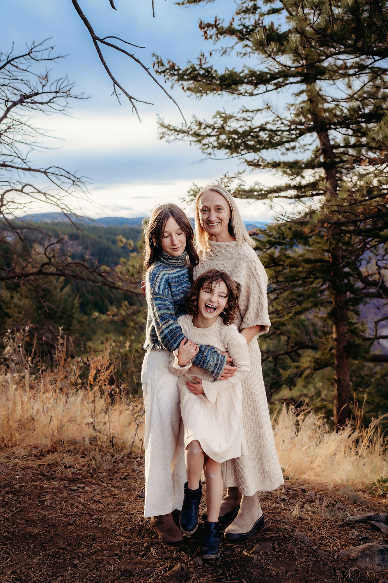 Mother with two children on a mountain overlook, wearing cozy neutral sweaters and dresses.