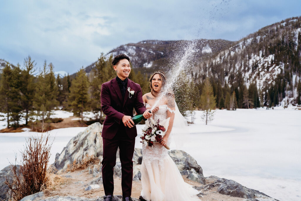 Colorado elopement photographer captures bride and groom celebrating recent marriage by popping champagne outdoors