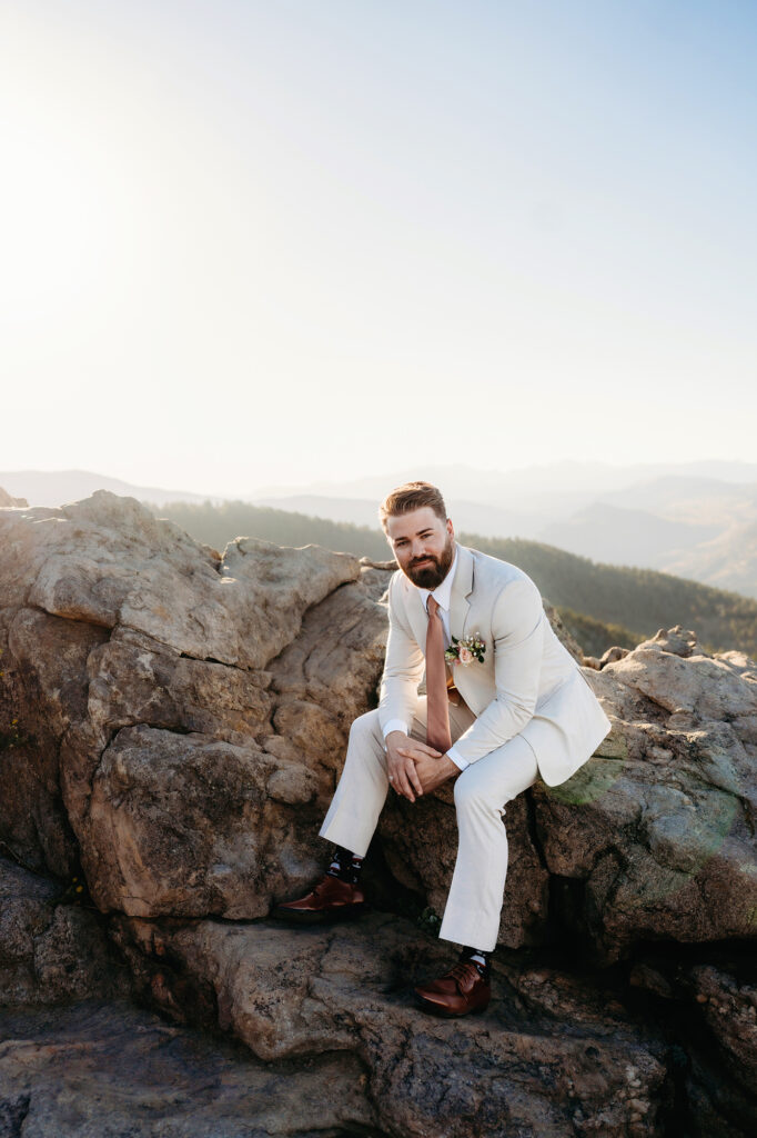 Colorado elopement photographer captures groom sitting on rock wearing wedding attire after wedding day hike