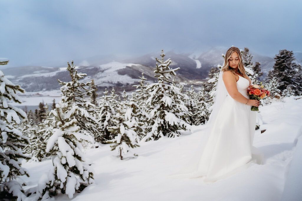 Colorado wedding photographer captures bride standing on snowy mountain holding bridal bouquet