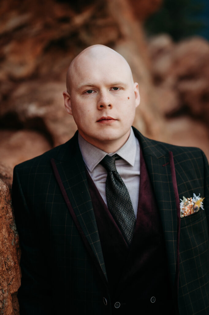 Denver Wedding Photographer captures groom standing against rock wearing black suit