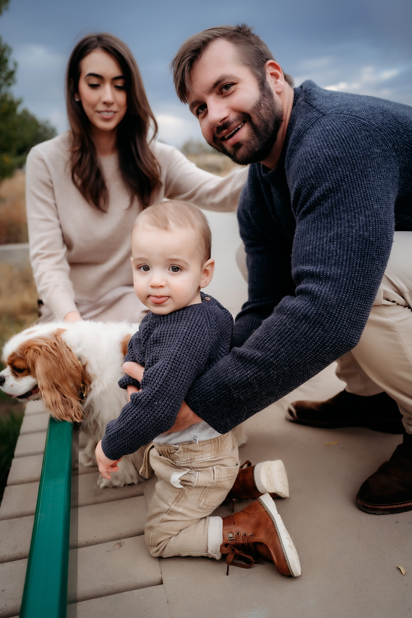 Parents crouching with their toddler and dog, dressed in casual navy and beige outfits for family photos.