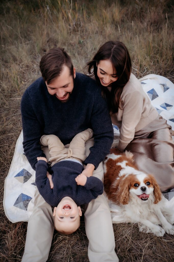 Denver Family Photographer captures mother and father playing with baby while dog sits near by during lifestyle family photos