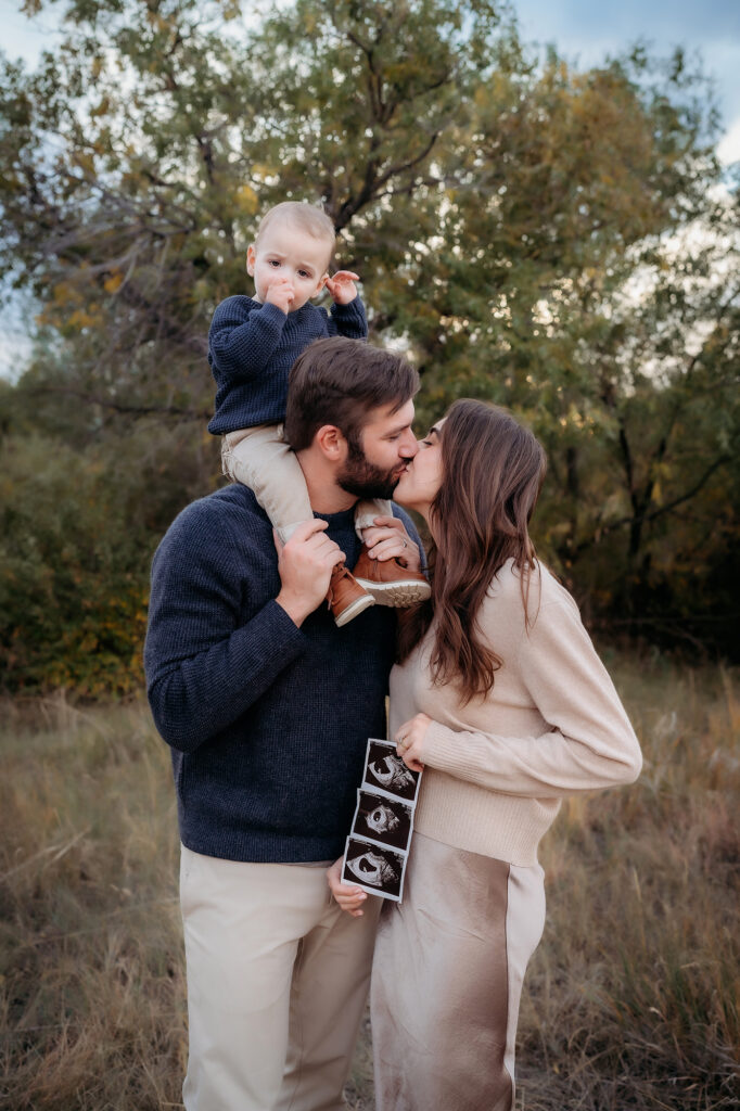 Denver Family Photographer captures husband and wife kissing during family photos announcing pregnancy