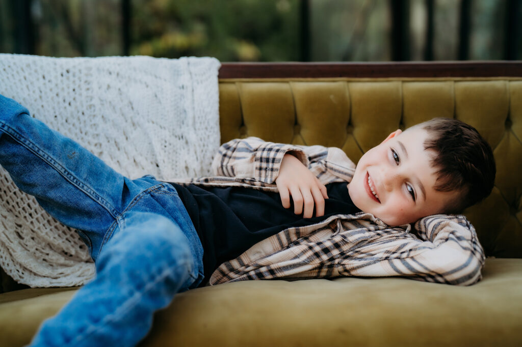 Denver Family Photographer captures young boy sitting on couch smiling during outdoor family photos