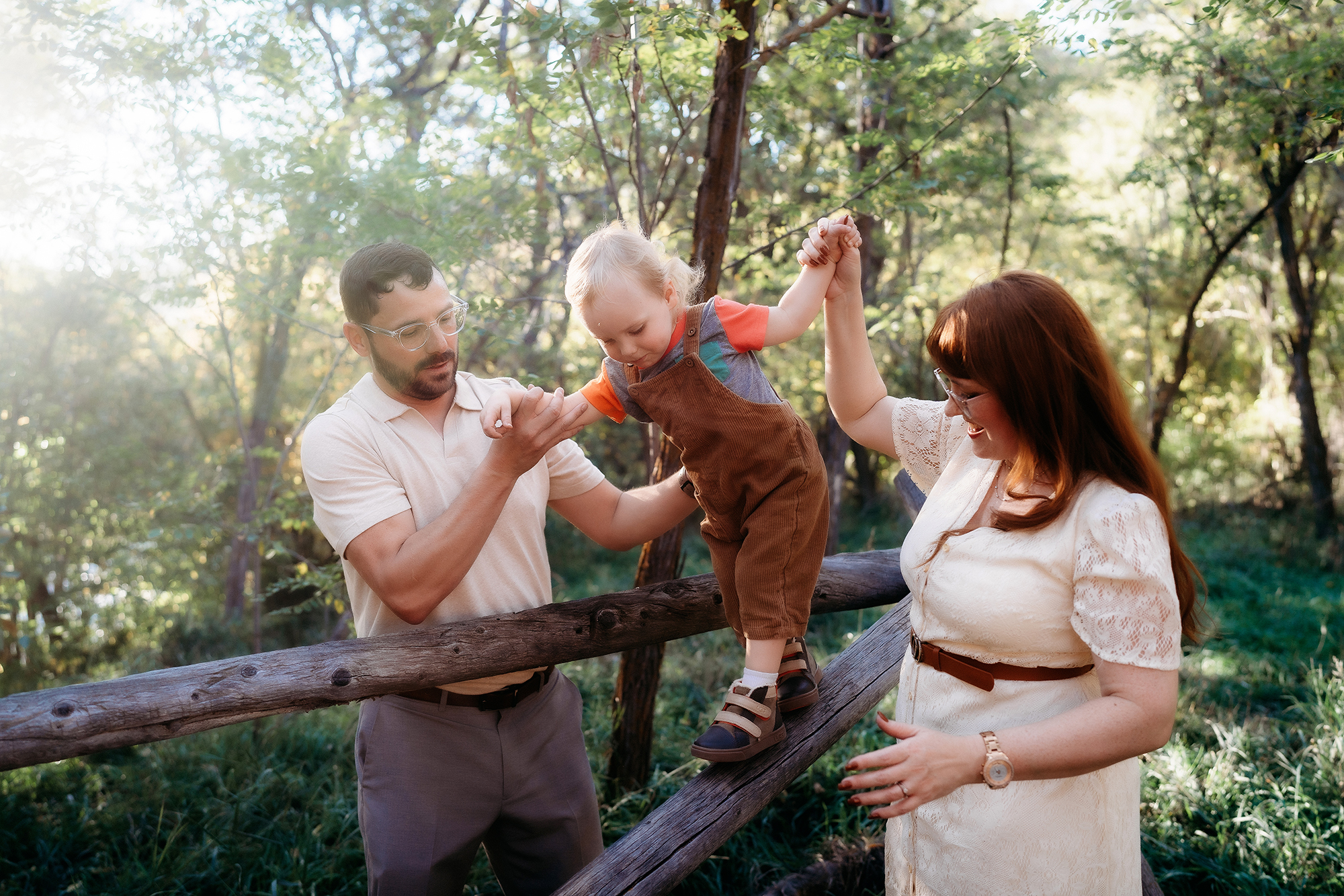 Denver Family Photographer captures mom and dad helping toddler walk along wooden beam