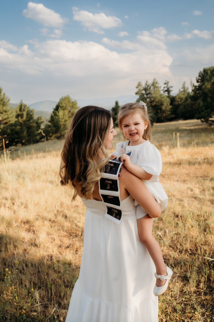 Denver Family Photographer captures mom holding daughter while daughter holds ultrasound pictures