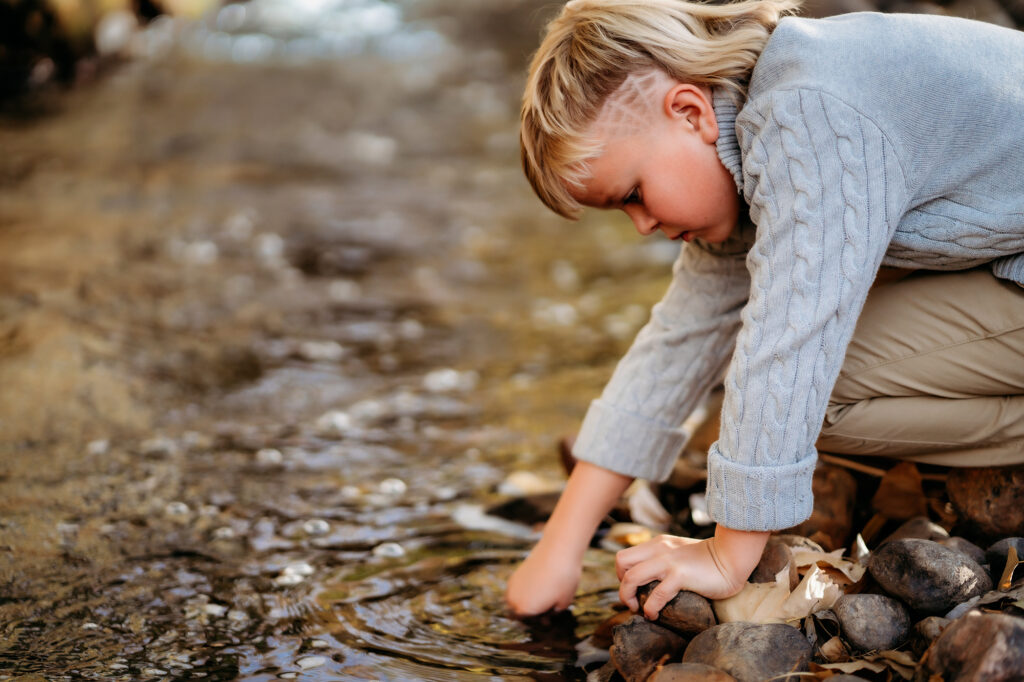 Denver Family Photographer captures young boy sticking hand in creek and exploring during themed-family photos