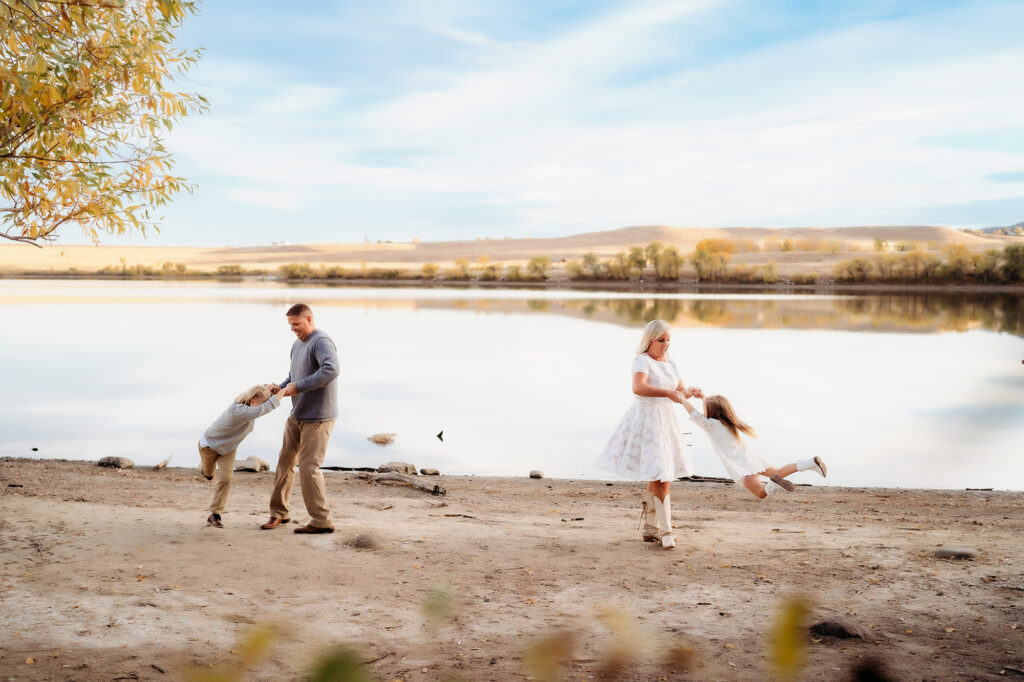 Denver Family Photographer captures mother and father swinging children and playing together during outdoor family photos in Denver