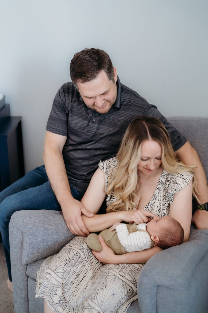 Denver Family Photographer captures mom sitting in chair holding baby while father looks on