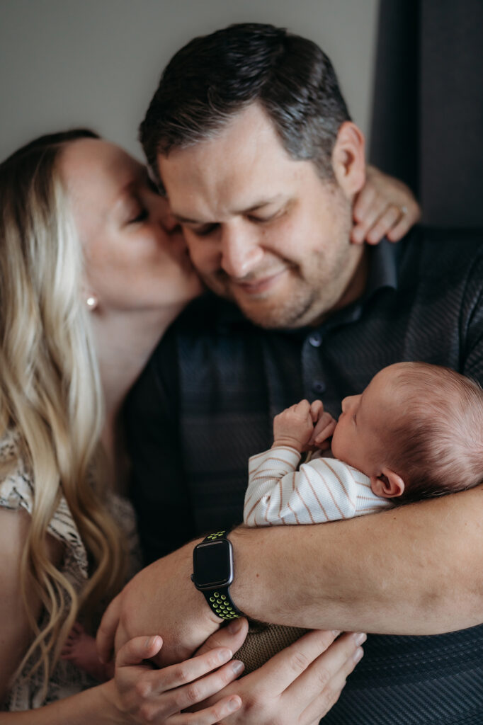 Denver Family Photographer captures wife kissing husband on cheek while holding baby