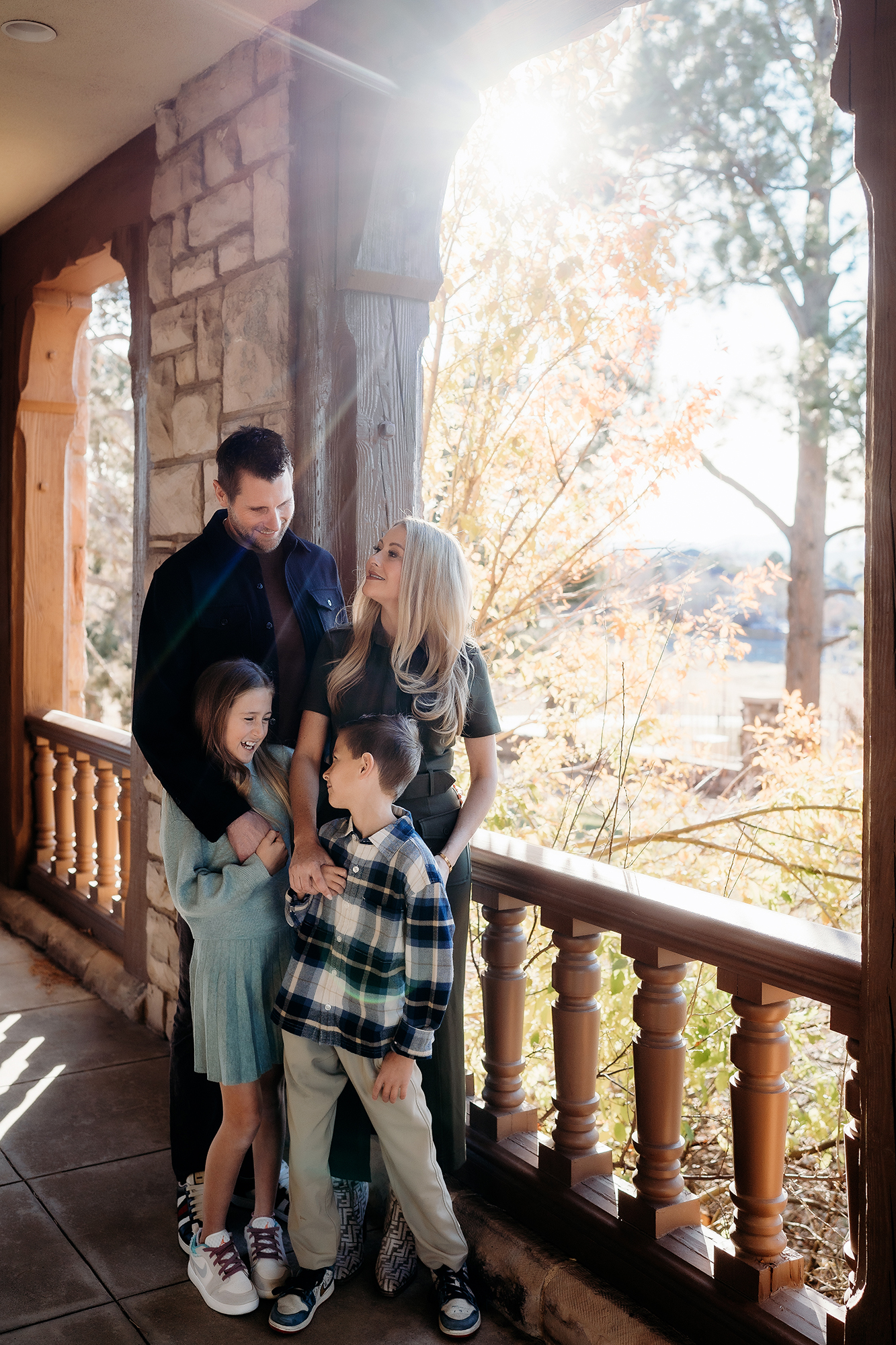 Family standing together on a porch in fall light, wearing plaid and soft cool-toned outfits.