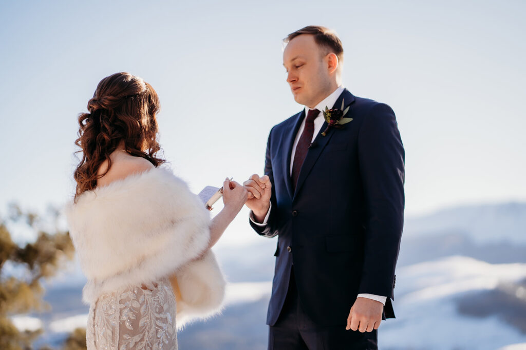 Bride reads vows while holding her groom’s hand, framed by alpine sunshine and soft snowfall—Colorado elopement photographer.