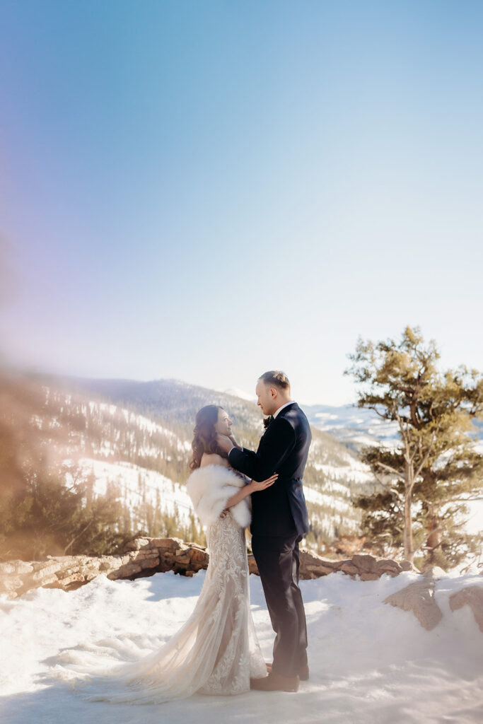 A gentle kiss shared by newlyweds with fresh snow and evergreen trees in the distance—Colorado elopement photographer.