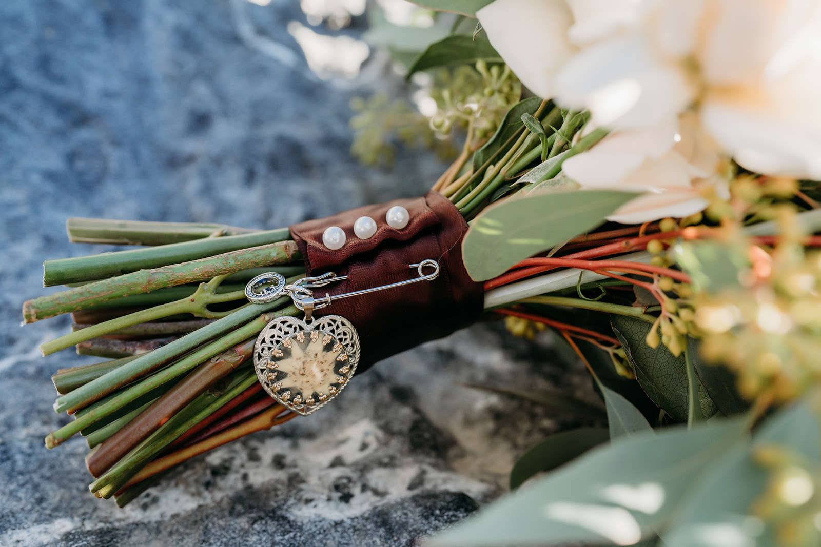 Detail shot of the bridal bouquet wrapped with pearl pins and heirloom charms, symbolizing something old and sentimental.