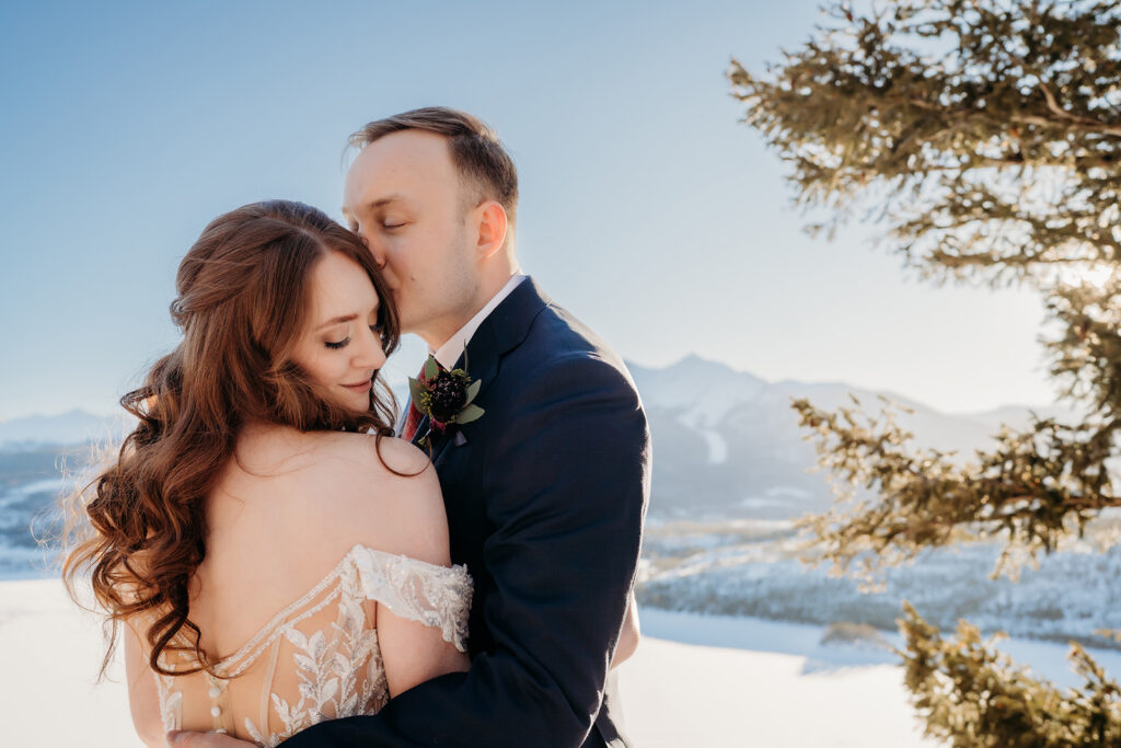 Groom kisses his bride’s temple as she smiles, wrapped in each other's warmth on the best day of your life.