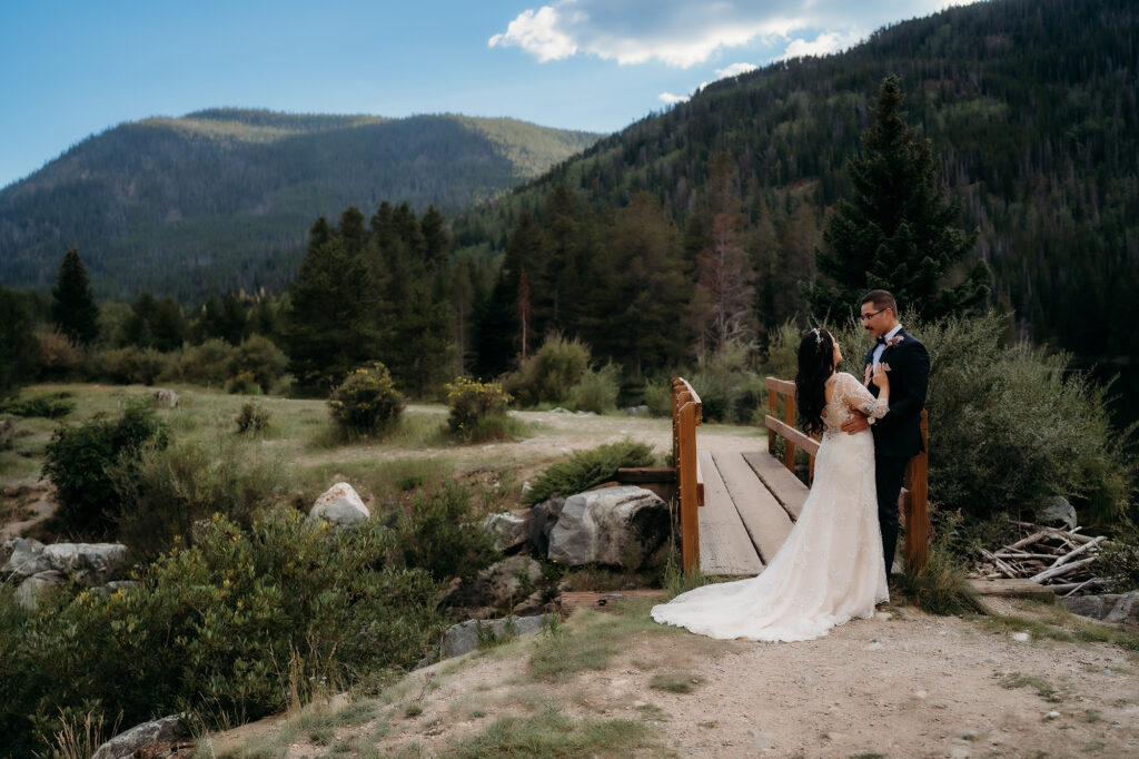 Couple walks hand-in-hand across a footbridge with sweeping views of forested Colorado hills — Colorado Elopement Checklist.