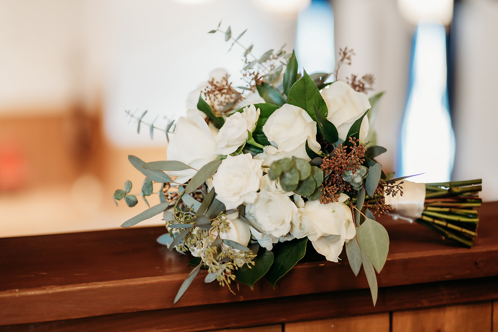Classic white rose bridal bouquet resting on a wooden ledge, a timeless floral choice for a small wedding in Colorado.