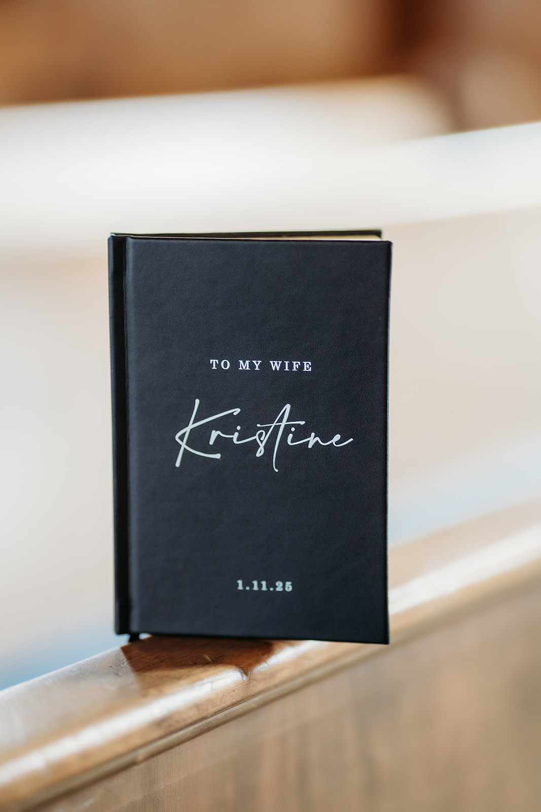 Custom vow book reading “To My Wife Kristine,” resting on a wooden pew before a small wedding in Colorado.