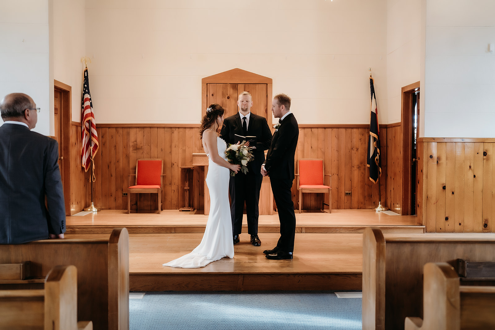 Bride and groom holding hands at the altar with the officiant between them, sharing vows in an intimate chapel setting.