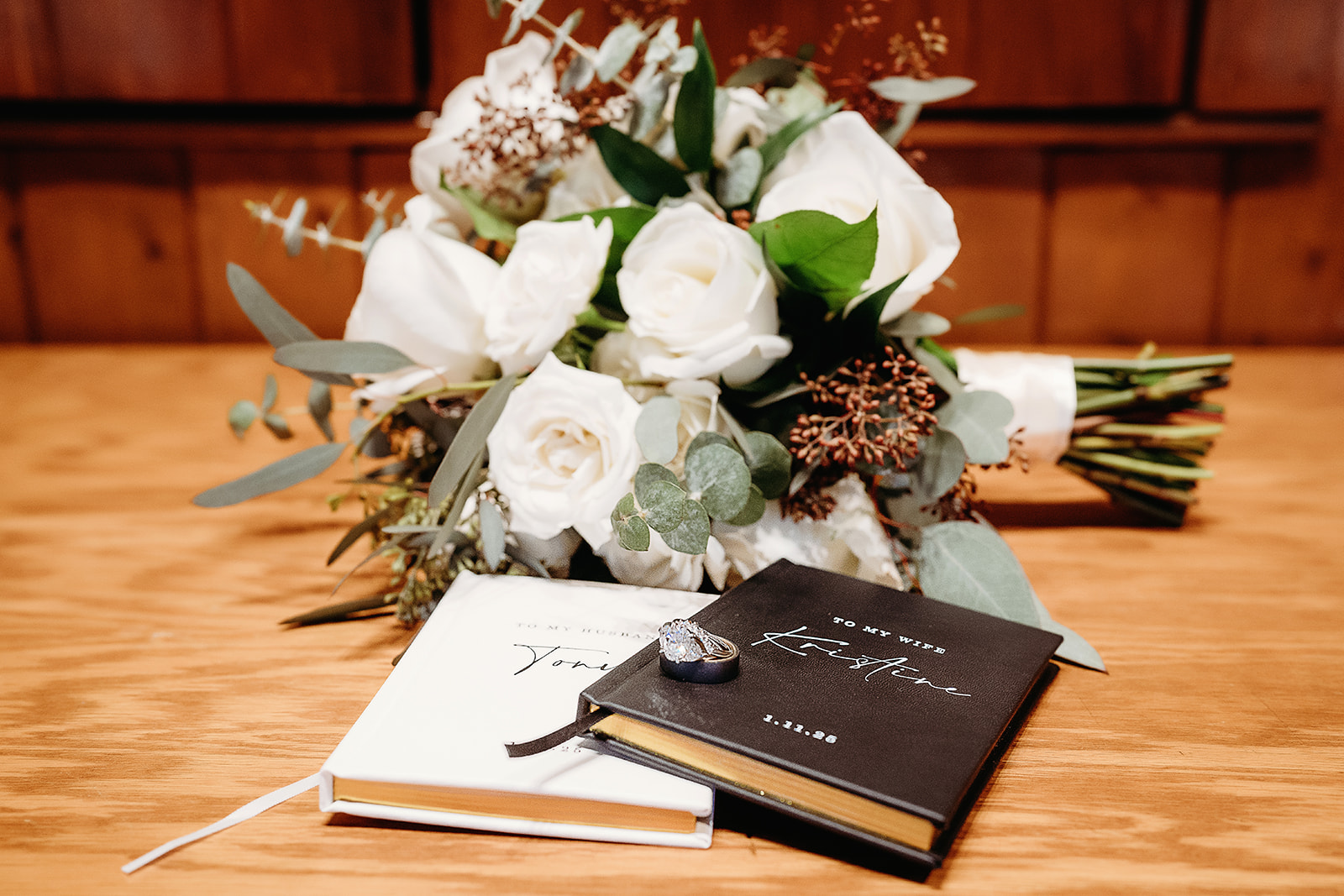 White rose bouquet paired with vow books and rings, styled beautifully on a wooden table post-ceremony.