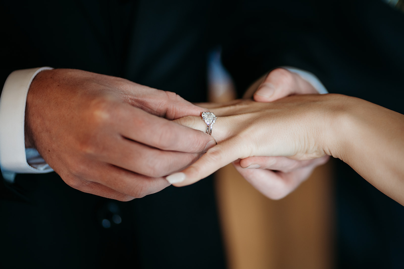 Close-up of groom gently placing the wedding ring on his bride’s finger during the ceremony.