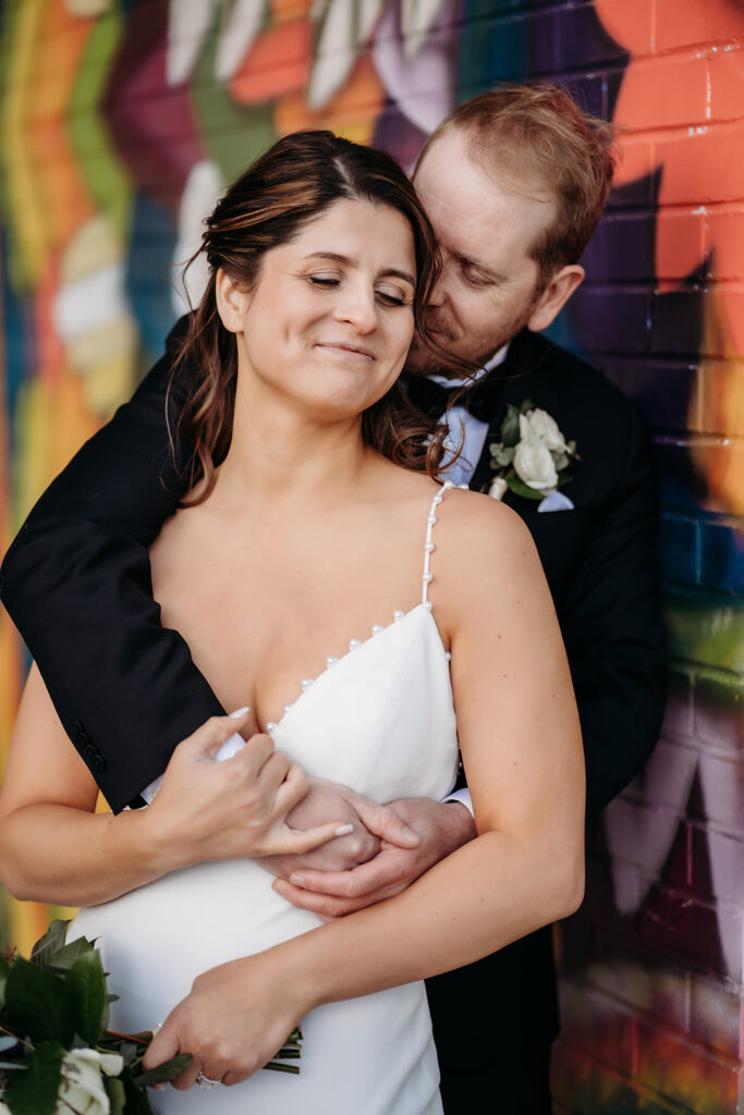Couple embraces in a quiet, affectionate moment in front of a colorful Denver mural wall.