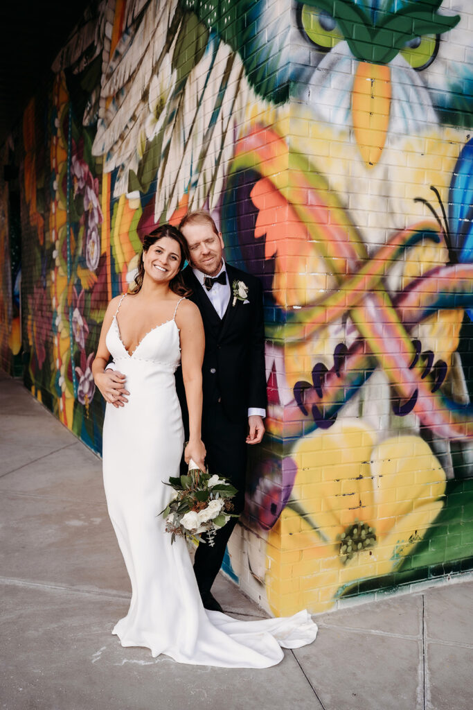 Bride and groom smiling together, framed by bold street art, capturing post-ceremony joy and connection.